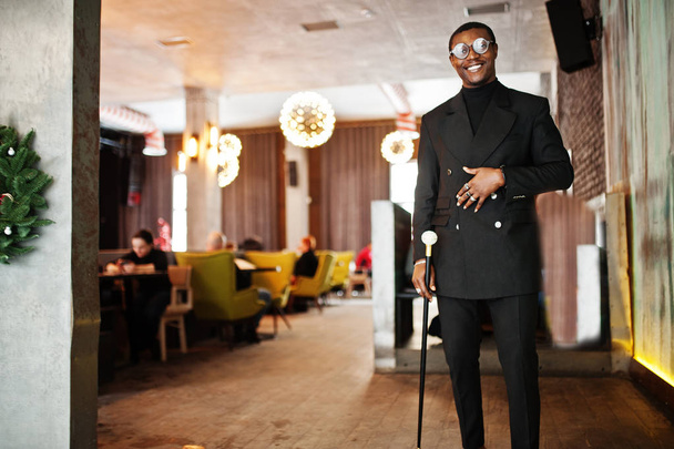 Stylish african american gentleman in elegant black jacket, holding retro walking stick as cane flask or tippling cane with golden diamond ball handle. Rich fashionable afro man. - Foto, Bild