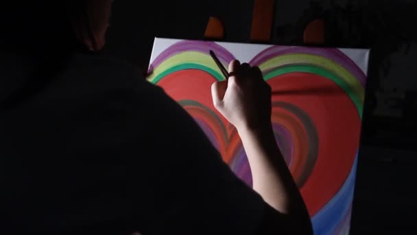 κοντινό πλάνο γυναίκα καλλιτέχνης ζωγραφική μια μεγάλη κόκκινη καρδιά στο καβαλέτο στο ατελιέ της στο σκούρο μαύρο φόντο - Πλάνα, βίντεο