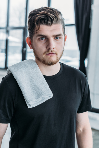 handsome young sportsman with towel on shoulder looking at camera in gym - Foto, Imagem