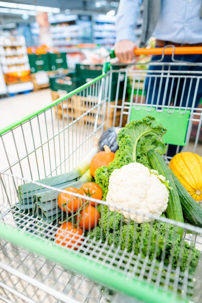 Hombre de compras en el supermercado empujando su carro con verduras
 - Foto, imagen