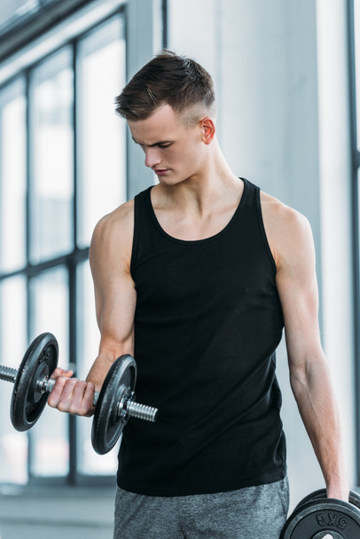 handsome young sportsman exercising with dumbbells in gym - Foto, Imagem
