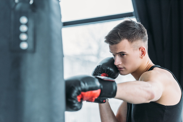 Jeune homme sportif concentré boxe avec sac de boxe dans la salle de gym - Photo, image