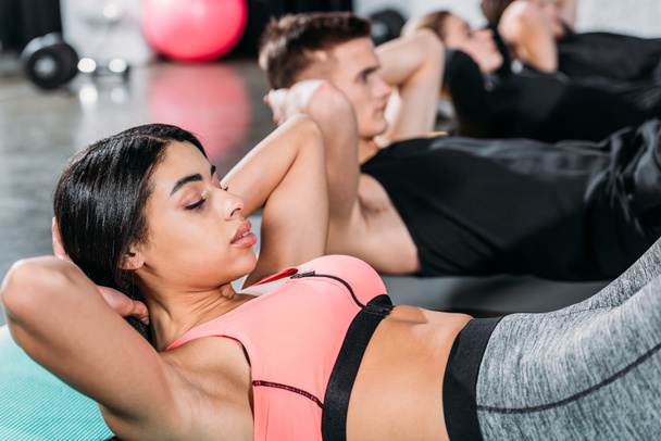 sportliche junge multiethnische Menschen, die auf Yogamatten liegen und im Fitnessstudio Bauch machen - Foto, Bild