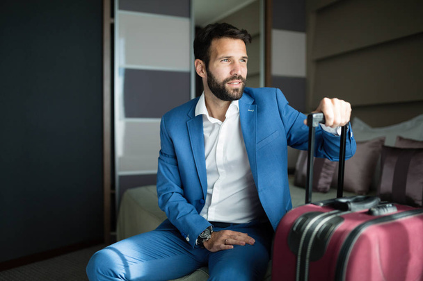 Portrait of handsome businessman in hotel room with luggage - Фото, изображение