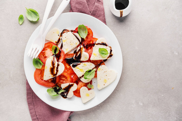 Italian classic caprese salad with heart shaped mozzarella, basil, balsamico and tomatoes served on plate - Foto, Imagen