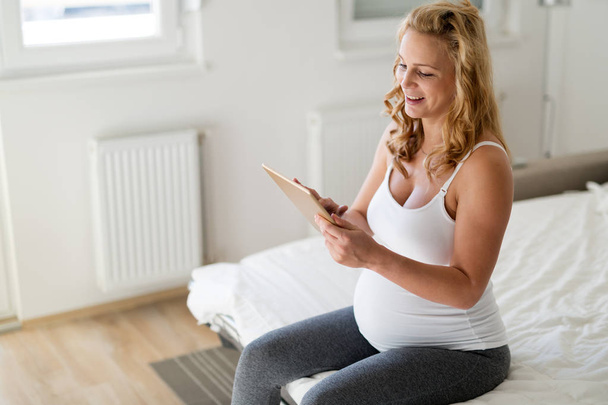Happy pregnant blonde woman using tablet in bedroom - Zdjęcie, obraz