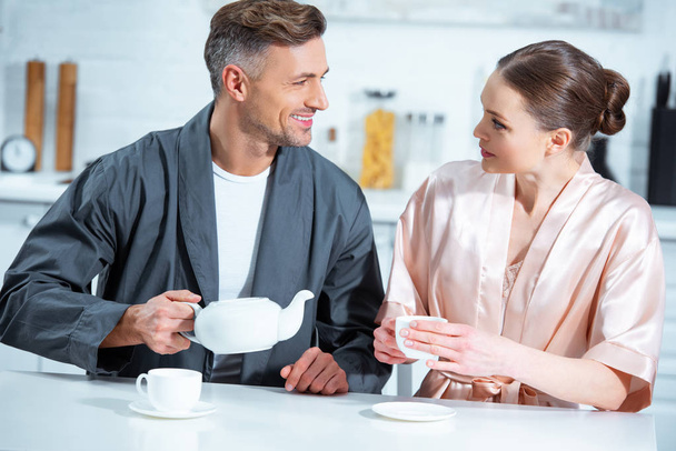 selective focus of beautiful adult couple in robes having tea in kitchen - Φωτογραφία, εικόνα