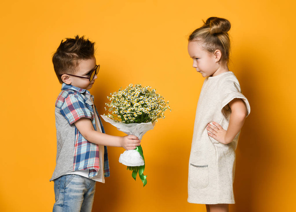 happy caucasian people boy gives a flowers to his girlfriend isolated over yellow background. - Photo, Image