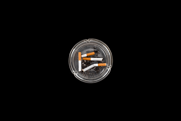 Vista superior del cenicero de vidrio con ceniza y cigarrillos aislados en negro
 - Foto, Imagen