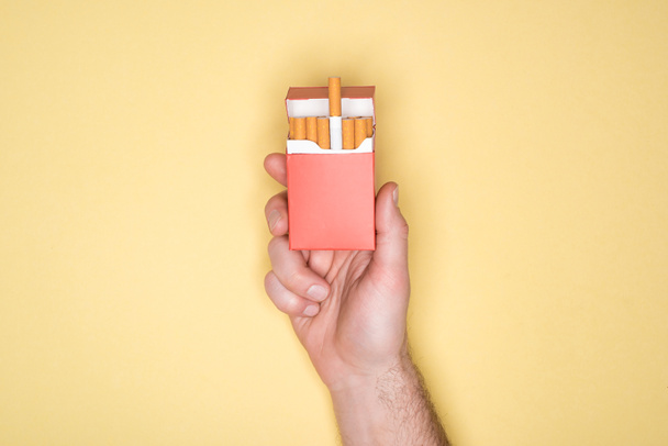 Vista recortada del hombre sosteniendo paquete rojo de cigarrillos aislados en amarillo
 - Foto, Imagen