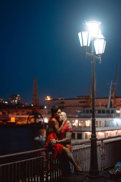 Τύπος και το κορίτσι που αγκαλιάζονται μεταξύ τους με φόντο το λιμάνι το βράδυ - Φωτογραφία, εικόνα