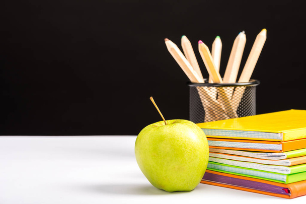 kleurrijke notebooks, potloden en appel geïsoleerd op zwart met kopie ruimte - Foto, afbeelding