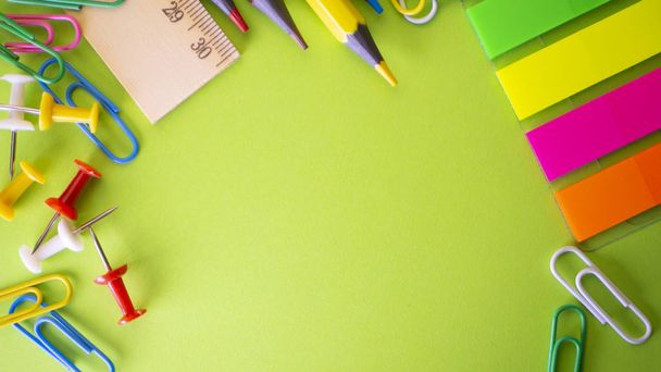 Schreibwaren auf grünem Hintergrund. Stifte, Bleistifte, Scheren, Büroklammern, Stecknadeln und auf dem Tisch. Blick von oben mit Kopierraum - Foto, Bild