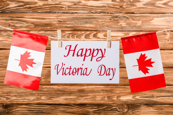 vista superior de bandeiras canadenses e cartão com letras 'happy victoria day' em fundo de madeira
 - Foto, Imagem