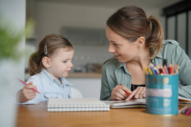 Mother and young daughter drawing and reading together at home - 写真・画像