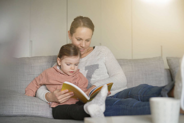 Mother and young daughter reading a story together at home - Foto, imagen