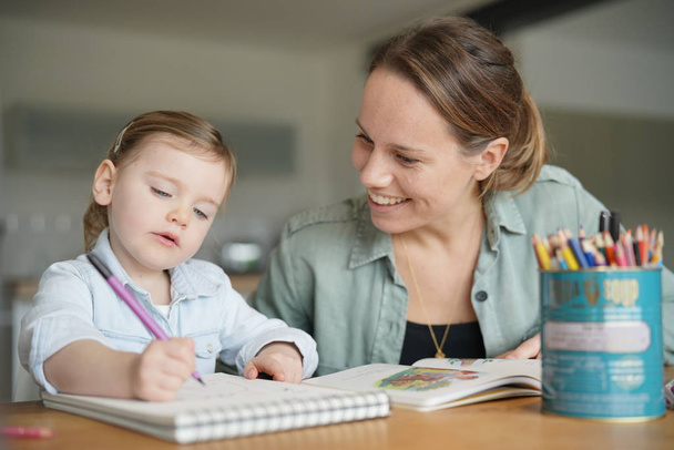 Mother and young daughter drawing and reading together at home - Foto, Bild