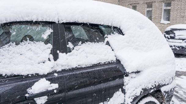 The car, covered with thick layer of snow. Negative consequence of heavy snowfalls. parked cars covered with snow during snowing in winter time - Photo, Image