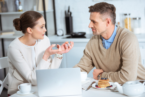 pareja adulta usando el ordenador portátil y tener conversación durante el desayuno por la mañana
 - Foto, imagen