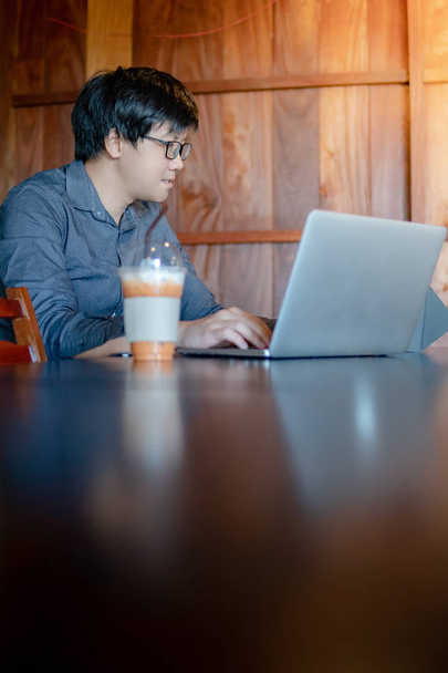 Homem de negócios asiático masculino usando óculos trabalhando com computador portátil moderno em mesa de madeira no café. Trabalho inteligente na era digital. Conceito de Internet das Coisas (IOT)
 - Foto, Imagem
