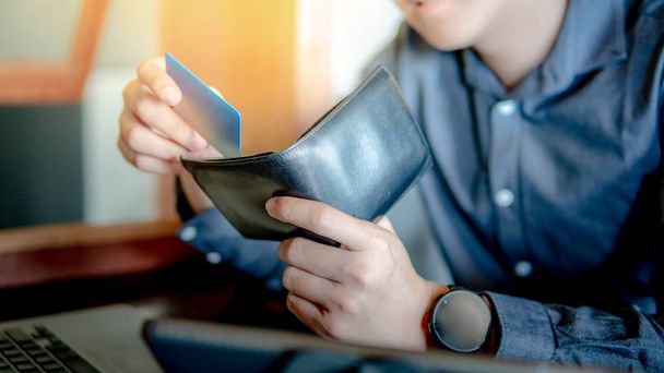 Αρσενική χέρι βάζοντας πιστωτική κάρτα στο πορτοφόλι του. Χρησιμοποιώντας την πιστωτική κάρτα για online αγορές σε φορητό υπολογιστή. Ψηφιακή πληρωμής και την κοινωνία χωρίς μετρητά έννοιες - Φωτογραφία, εικόνα