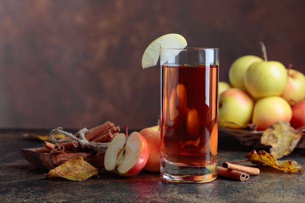 Glass of apple juice or cider with juicy apples and cinnamon sticks on a kitchen table. - Photo, Image
