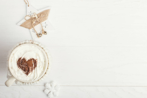 A cup of hot winter drink with whipped cream and a dusting powder with an asterisk, white snowflakes on a wooden table. Christmas concept in bright colors. Copy space. - Foto, Bild