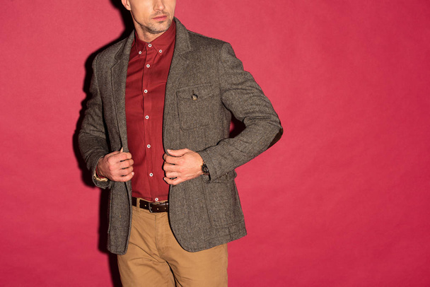 cropped view of stylish man in formal wear adjusting jacket on red background - Foto, imagen