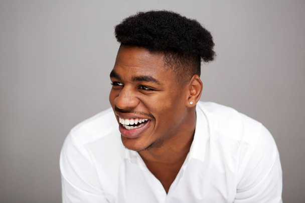 Nahaufnahme Porträt eines hübschen jungen afrikanisch-amerikanischen Mannes, der vor grauem Hintergrund lacht und wegsieht - Foto, Bild