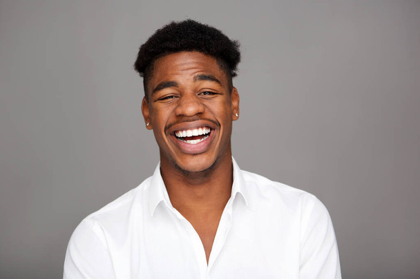 Close-up van portret van knappe jonge zwarte man lachen tegen de grijze achtergrond - Foto, afbeelding