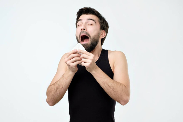 Hispanic young man with black beard being ill sneezing. Grippe and or allergy problem - 写真・画像