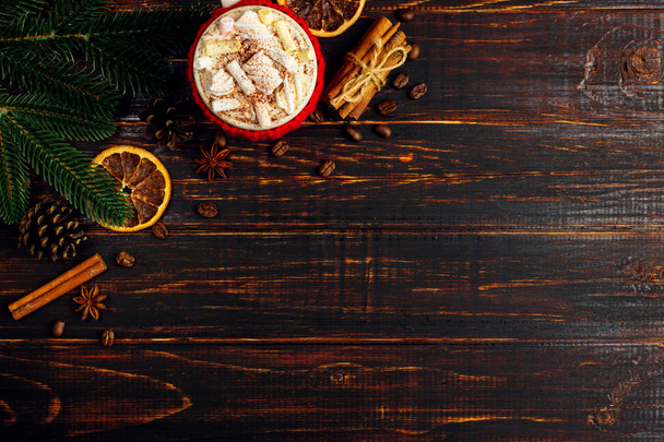 Ένα φλιτζάνι ζεστό ρόφημα με κρέμα σαντιγί, marshmallows και σκόνη, σε ένα πλεκτό κάλυμμα και σπιτικά κουλουράκια, κανέλα, Χριστούγεννα διακόσμηση, βρίσκονται πάνω στο ξύλινο τραπέζι. Χώρο αντίγραφο. - Φωτογραφία, εικόνα