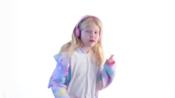 moderne mode - mooi blond meisje luistert naar muziek met hoofdtelefoons en dansen op een witte achtergrond in kigurumi pyjama - geïsoleerd op wit - Video