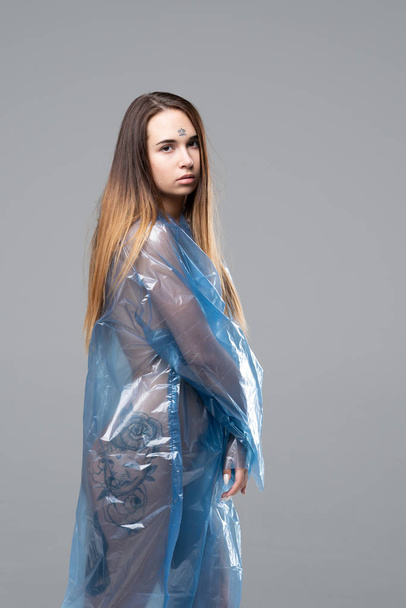 young beautiful girl posing in the studio, standing in a blue raincoat - 写真・画像