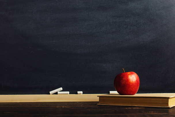 Μαύρη κιμωλία σανίδα πάνω από ξύλινο τραπέζι με ένα βιβλίο και ένα μήλο, κενό για το κείμενο ή φόντο για ένα σχολικό θέμα. - Φωτογραφία, εικόνα