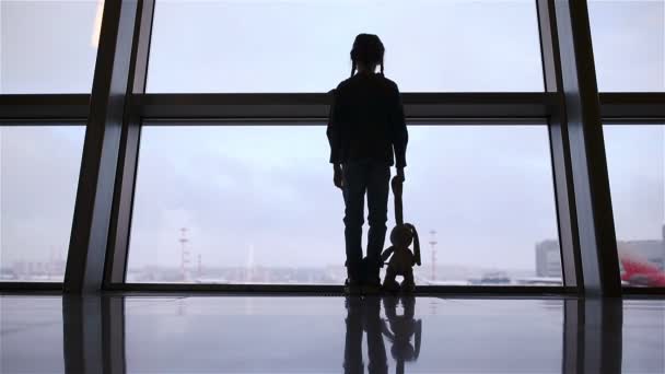 Mała dziewczynka na lotnisku w pobliżu dużego okna podczas oczekiwania na wejście na pokład - Materiał filmowy, wideo
