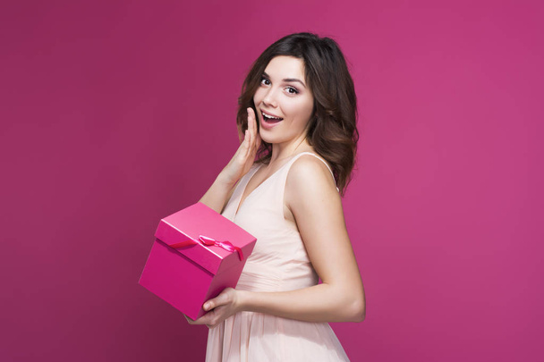 surprised brunette in a dress with a gift in hand - Фото, изображение