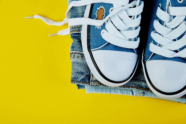 Blue female or male sneakers and jeans, denim  on yellow paper background. Flat lay. Top view. Minimal background. Fashion blog or magazine concept. Copy space. Trendy - Foto, Imagem
