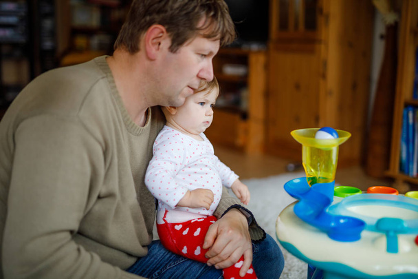 Ευτυχισμένος περήφανος νεαρός πατέρας διασκεδάζοντας με μωρό κόρη, οικογενειακό πορτρέτο μαζί. Μπαμπάς παίζει με μωρό κορίτσι με εκπαιδευτική ταξινόμηση παιχνιδιών με διάφορες πολύχρωμες μπάλες. Άνθρωπος με μικρό παιδί στο σπίτι. - Φωτογραφία, εικόνα