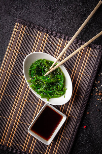 The concept of Japanese and Chinese cuisine. Chuka Salad, made from seaweed, sesame, olive oil and spices. soy sauce and chinese sticks on a black background. top view, flat lay - Fotoğraf, Görsel