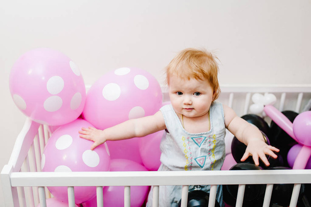 Little baby girl infant playing in bed decorated colored balloons for birthday party - Foto, imagen