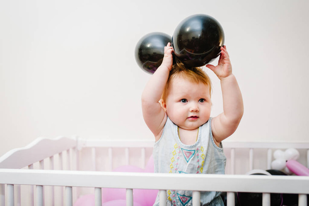 Little baby girl infant playing in bed decorated colored balloons for birthday party - Φωτογραφία, εικόνα
