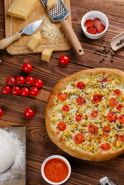 vista superior de la pizza cocida con salsa blanca, queso y tomates en rodajas en la mesa de madera
 - Foto, imagen