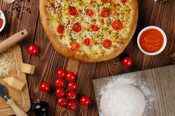 ahşap masa üzerinde beyaz sos, peynir ve dilimlenmiş domates ile pişmiş pizza üstten görünüm - Fotoğraf, Görsel