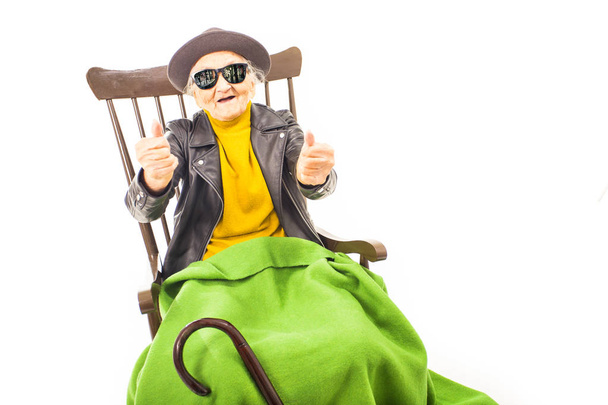 Old woman with hat and sunglasses sitting on the chair coverd with green blacket. - Fotoğraf, Görsel