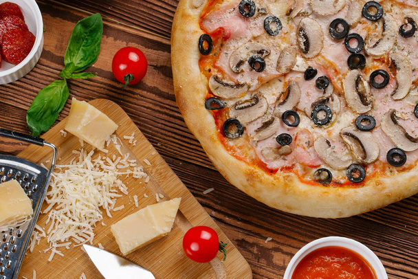 bovenaanzicht van gekookte pizza met tomatensaus, kaas, gesneden spek, champignons en olijven - Foto, afbeelding