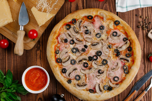ylhäältä näkymä keitettyä pizzaa tomaattikastikkeella, juustolla, viipaloidulla pekonilla, sienillä ja oliiveilla
 - Valokuva, kuva
