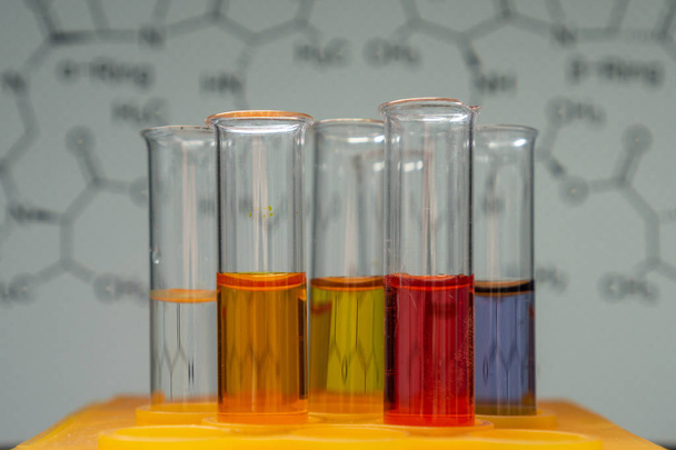 test tubes with liquid colored chemicals in a mount, chemical structure formula in the background - Photo, Image