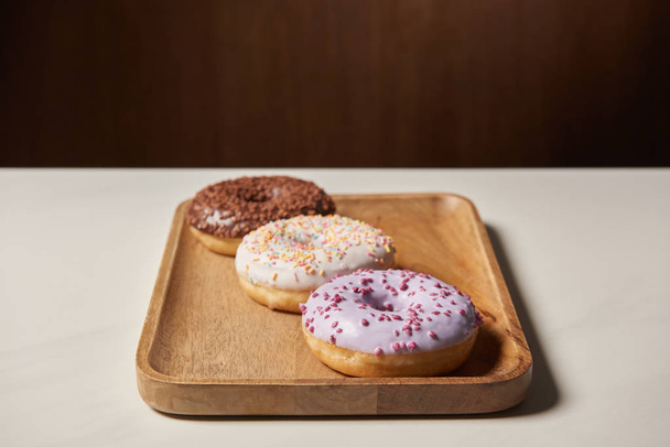 sweet glazed doughnuts with sprinkles on wooden cutting board - Foto, afbeelding