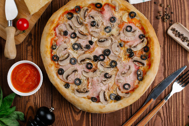 bovenaanzicht van gekookte pizza met tomatensaus, kaas, gesneden spek, champignons en olijven - Foto, afbeelding